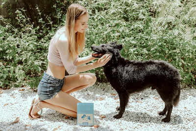 a woman kneeling down next to a black dog